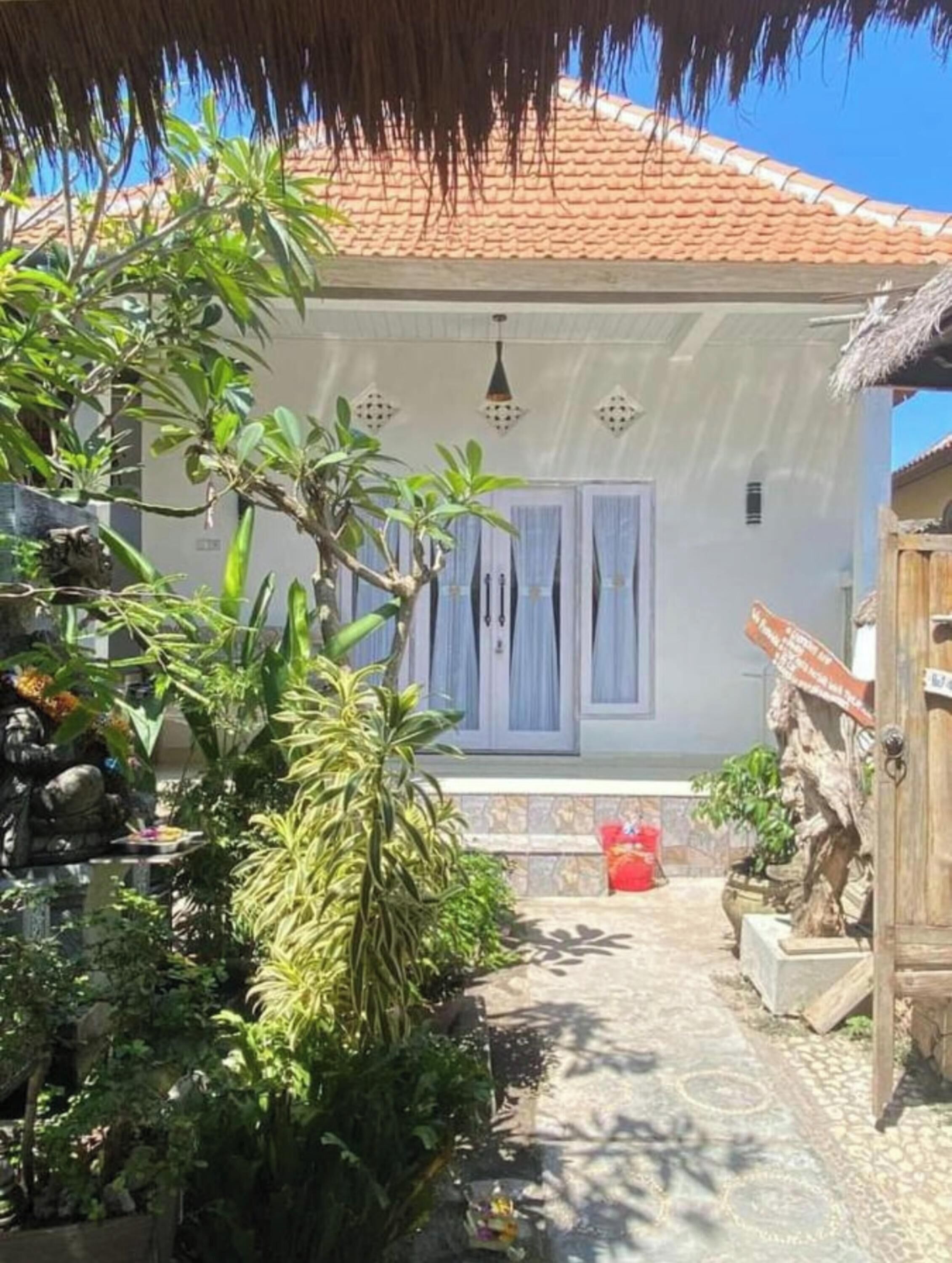 A house with a tiled roof, a thatched roof structure, and a garden with various plants.