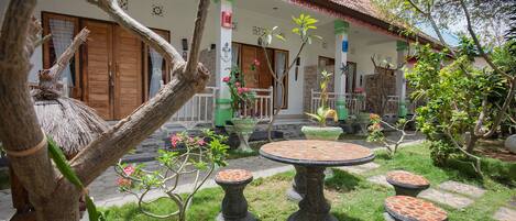 A courtyard with a thatched-roof structure, a stone table with four stools, and a variety of potted plants.