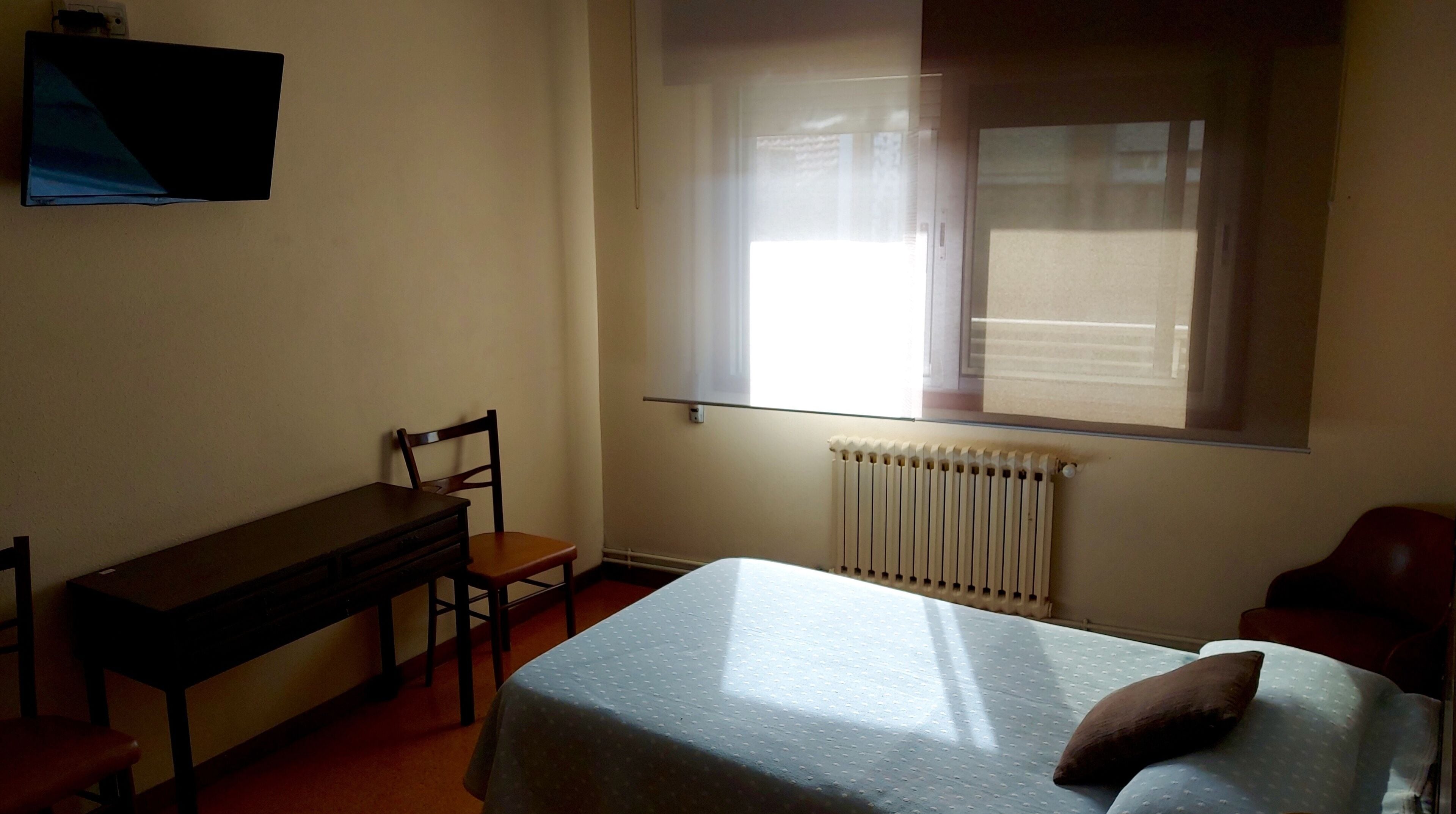 Une chambre avec un lit, un bureau, une chaise et une fenêtre avec des stores.