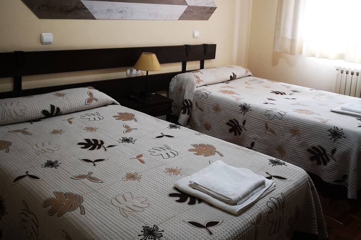 A hotel room with two beds, each with floral-patterned bedding, a large abstract wall art piece, and a window with curtains.