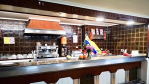 A restaurant counter with a coffee machine, a cash register, and a decorative flag. - Hostal Louro (O Porrino)