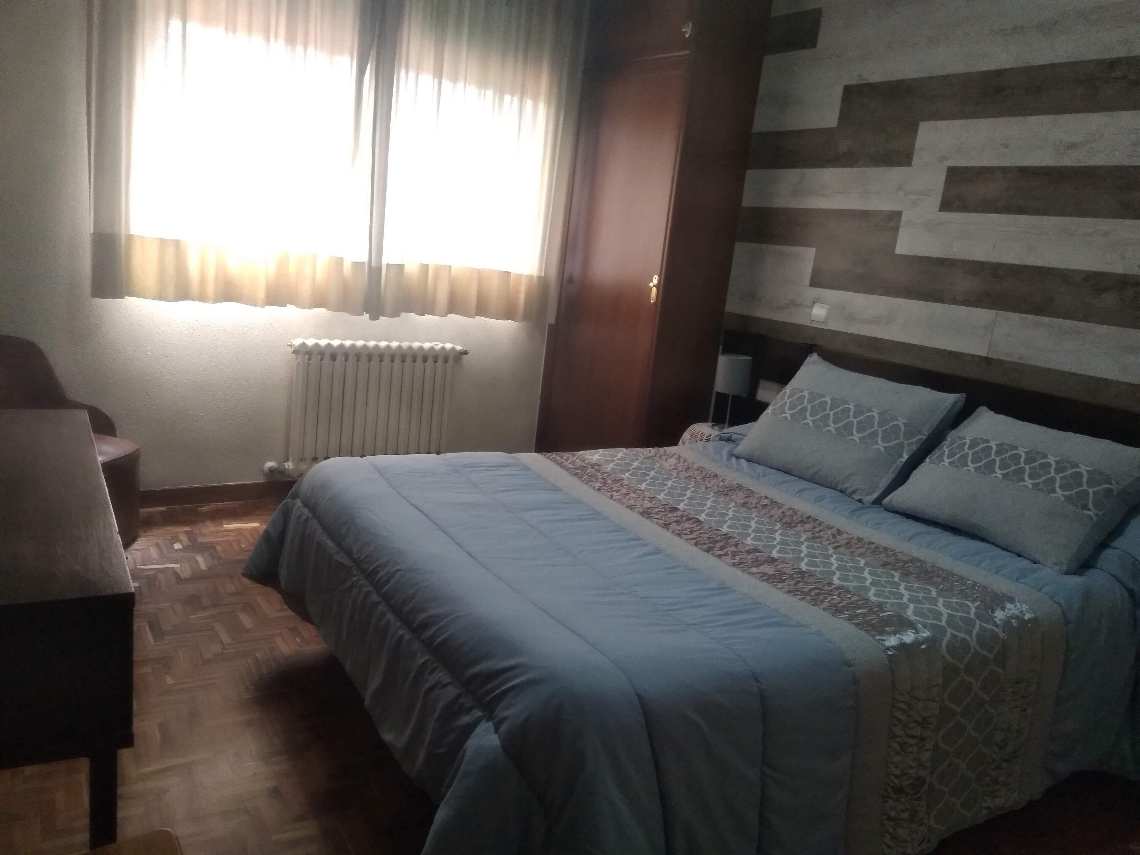 A bedroom with a bed, a chair, a radiator, and a window with curtains.