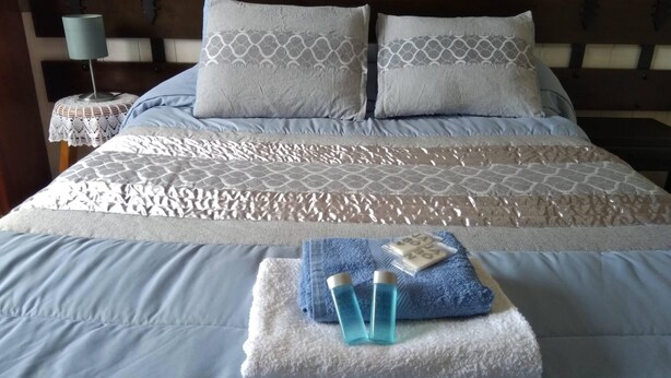 A neatly made bed with a patterned bedspread, two pillows, and a folded towel with toiletries on a bedside table. - Hostal Louro (O Porrino)