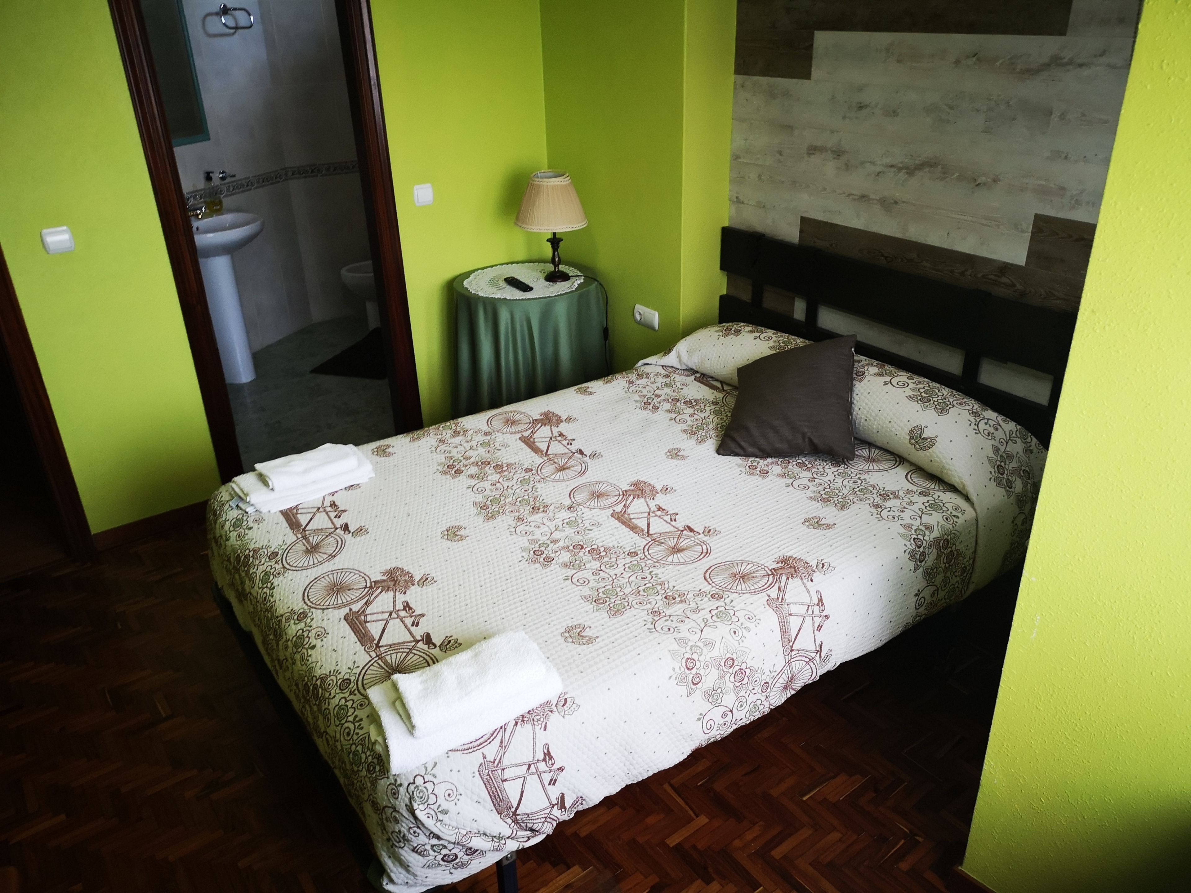 Una cama con colcha estampada, una lámpara de noche y una almohada.