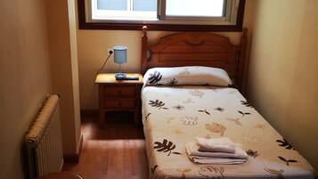 Un dormitorio pequeño con una cama individual, una mesita de noche, un escritorio con lámpara y un radiador.