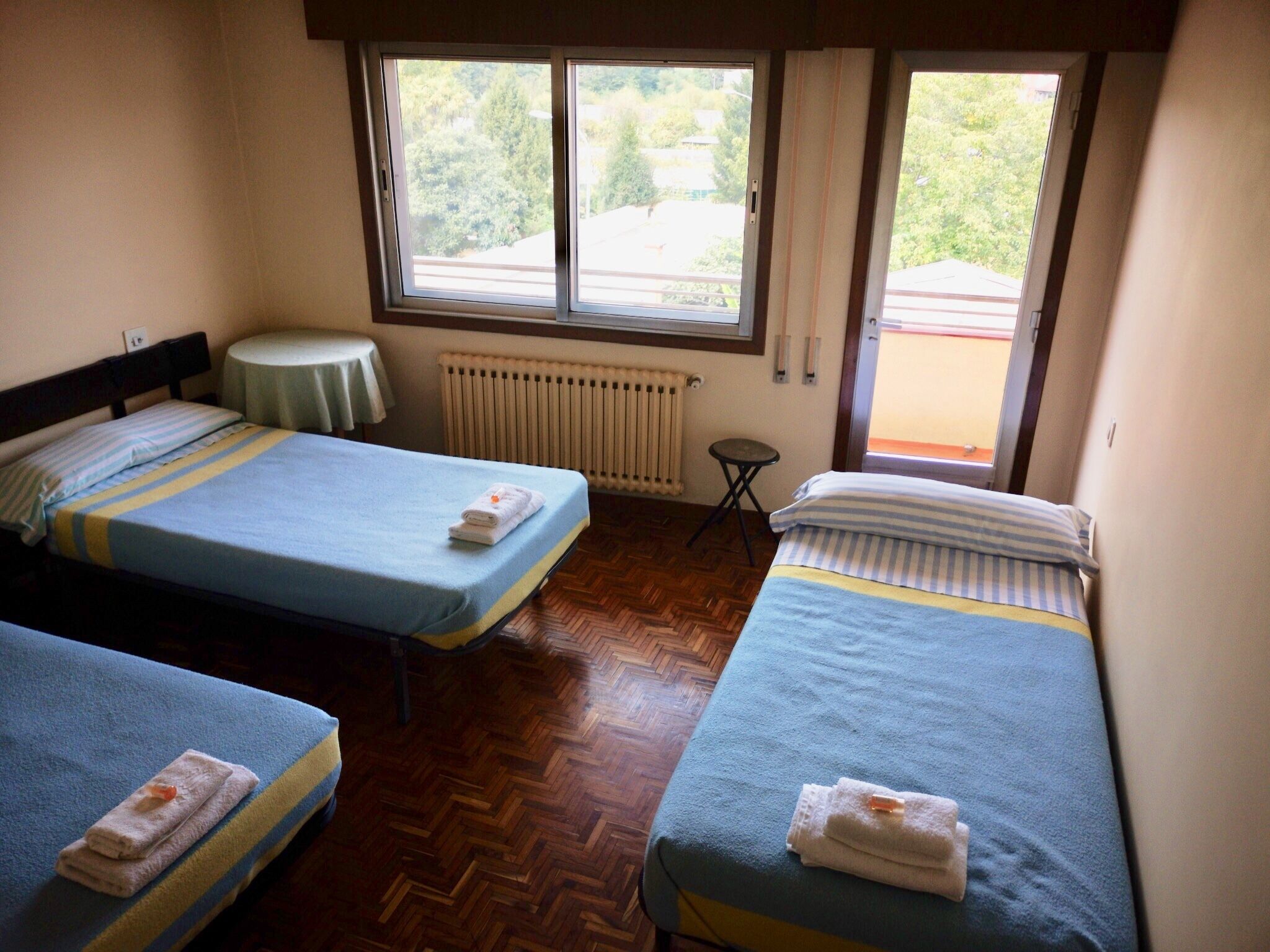 Una habitación con dos camas, una mesita redonda y un ventanal con vistas a zonas verdes.