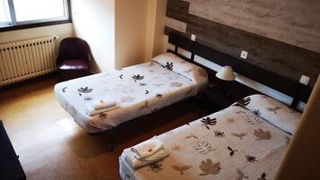 A room with two single beds, a radiator, a chair, and a lamp.