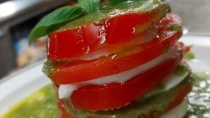 A layered dish with tomatoes, cheese, and a green sauce, served on a white plate. - Hostal Louro (O Porrino)