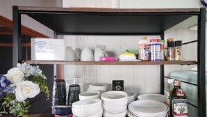 A kitchen shelf with various kitchenware, including plates, bowls, and a bottle of olive oil. - Terrace House Tsubokawa (Naha)