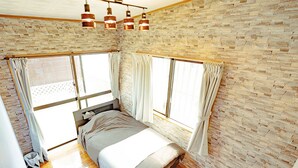 A bedroom with a brick wall, large windows, a bed, and a ceiling light fixture. - Terrace House Tsubokawa (Naha)