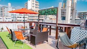 An outdoor patio with wicker furniture, a hammock, and a red umbrella. - Terrace House Tsubokawa (Naha)