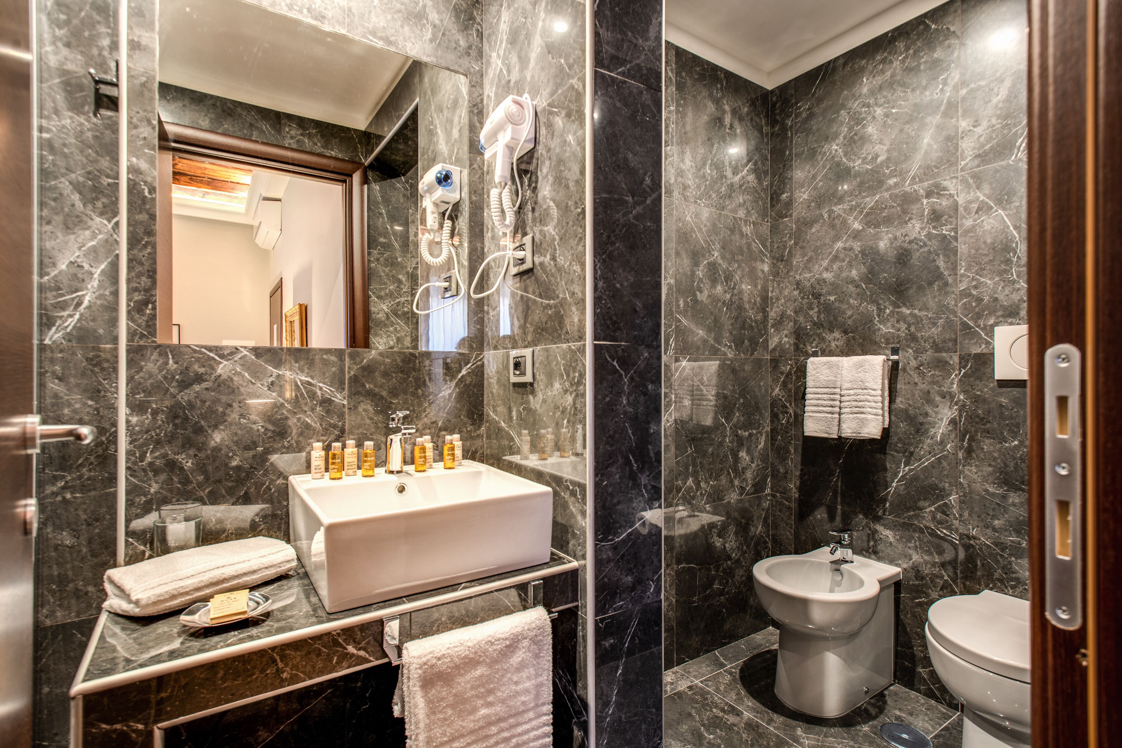 Et moderne badeværelse med vask i marmor, en bidet og et spejl.