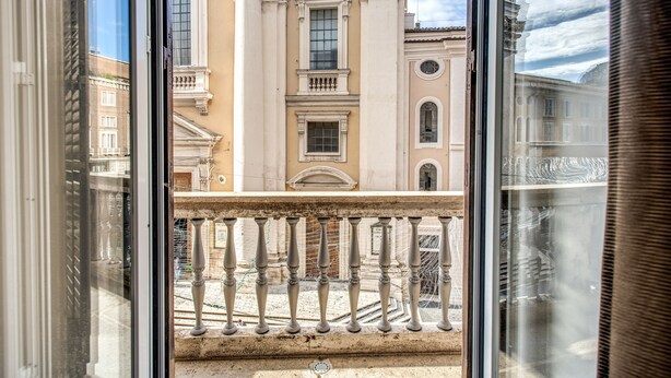 Vista da janela de um edifício com arquitetura clássica, destacando colunas e uma varanda.