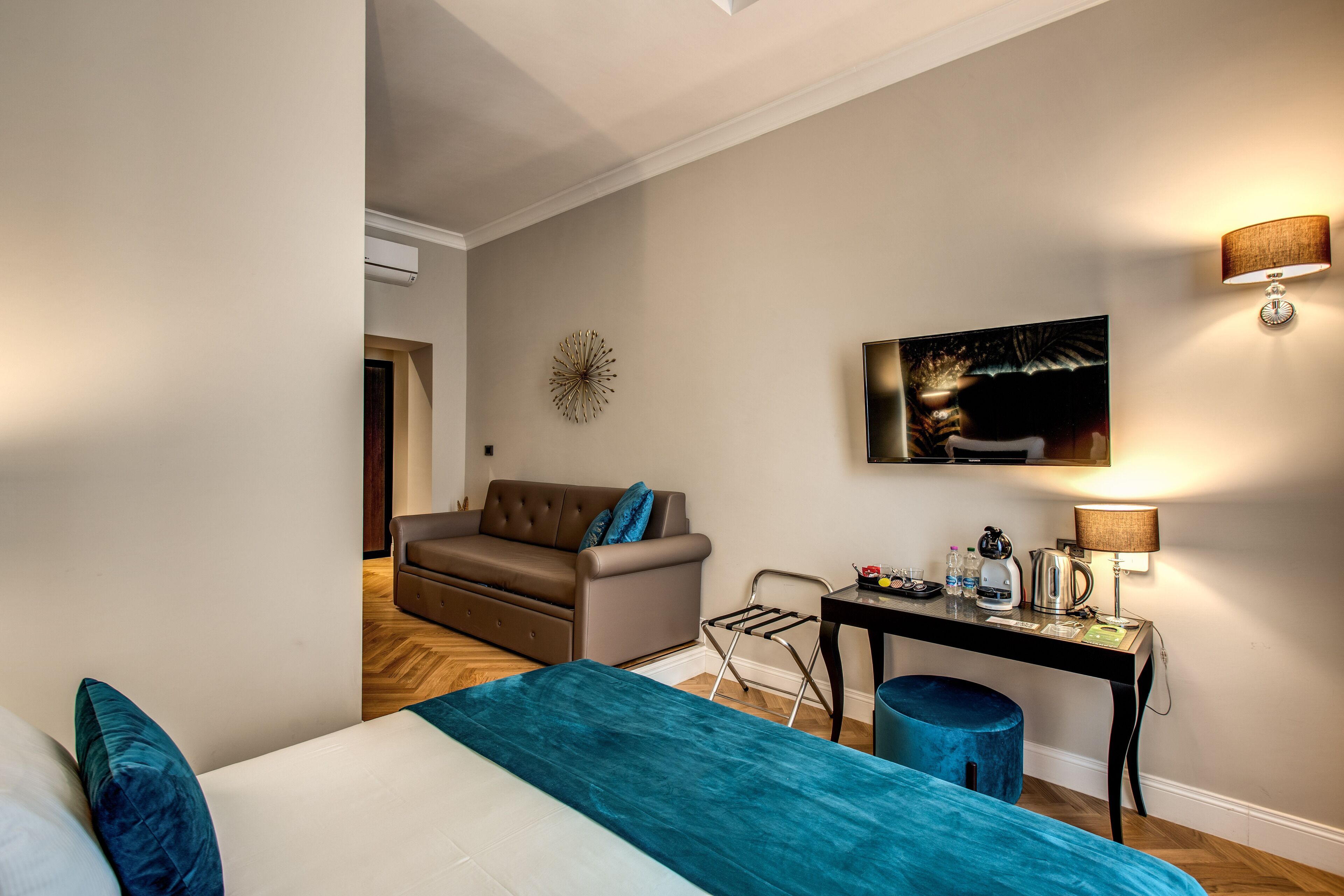 A modern hotel room with a bed, a sofa, a coffee table, and a wall-mounted TV.