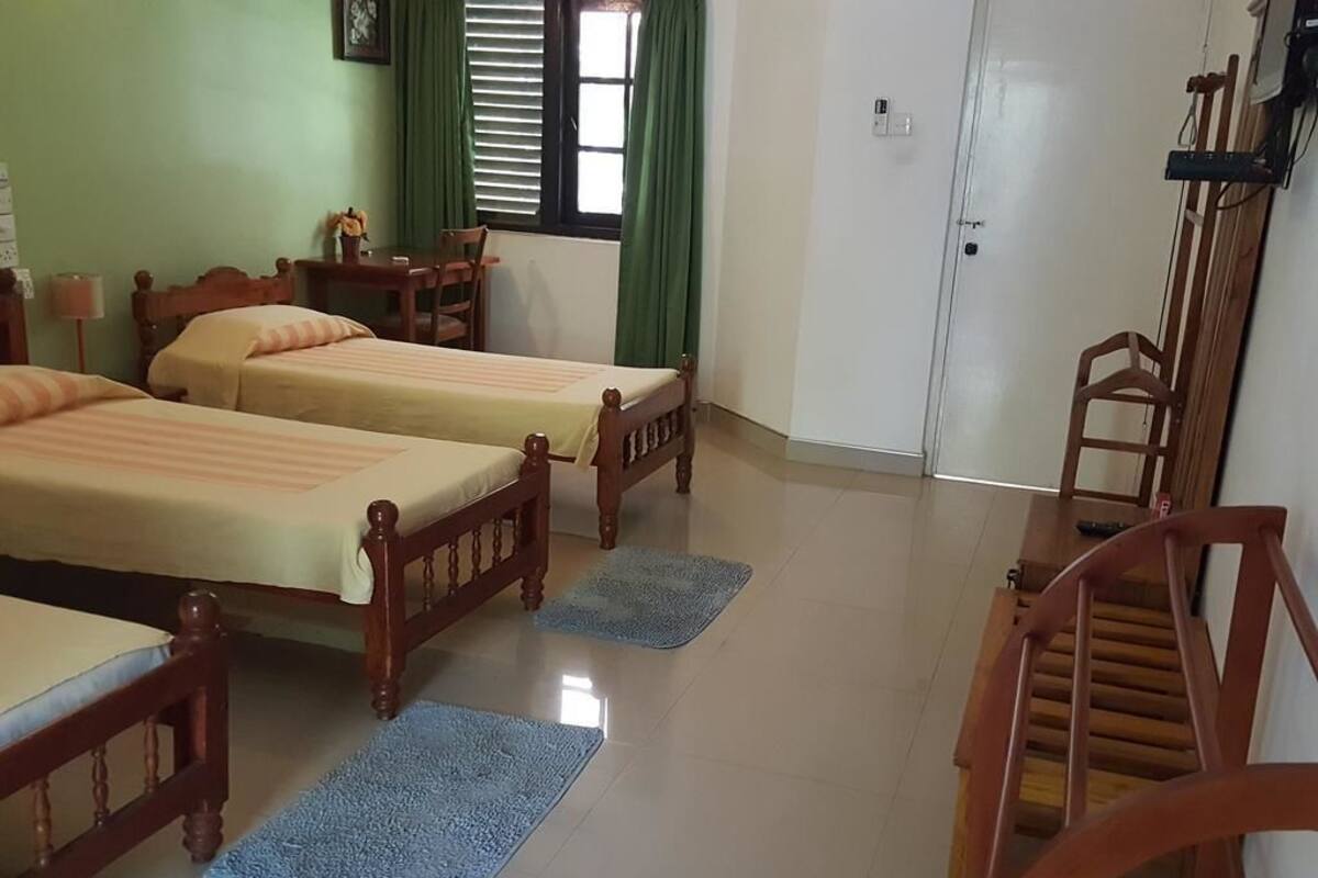 A room with two wooden beds, a desk with a chair, a wardrobe, and a wooden chair.