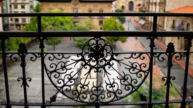 A balcony with ornate metal railings overlooking a street with buildings and a church tower. - Soho Boutique Oviedo  (Oviedo)