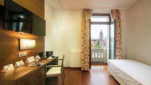 A hotel room with a wooden desk, a bed, a television, and a view of a building through the window. - Soho Boutique Oviedo  (Oviedo)