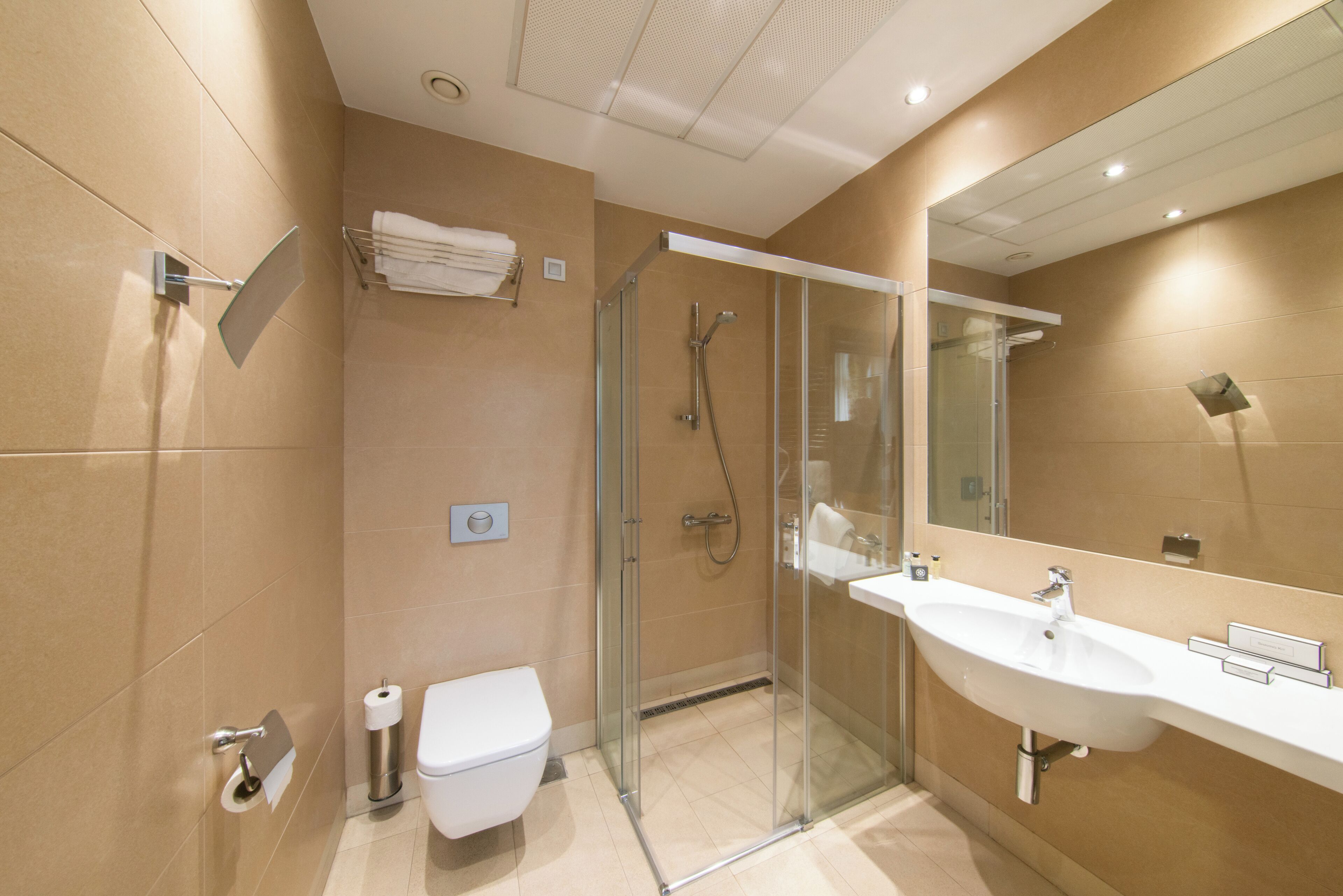 Un baño moderno con ducha de mampara de vidrio, lavabo blanco y retrete.
