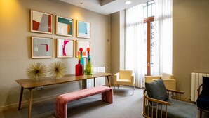 A modern living room with a wooden bench, a yellow armchair, and a blue armchair. There are framed artworks on the wall and a table with decorative bottles. - Soho Boutique Oviedo  (Oviedo)
