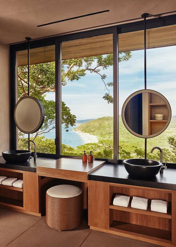 Un bagno con due lavandini, una grande finestra e vista sulla spiaggia.