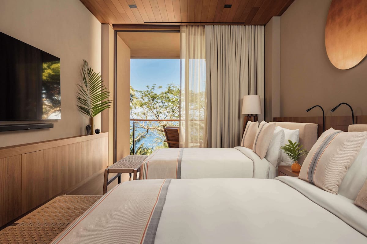 Una habitación de hotel moderna con dos camas, un televisor, un balcón con vistas y un techo de madera.
