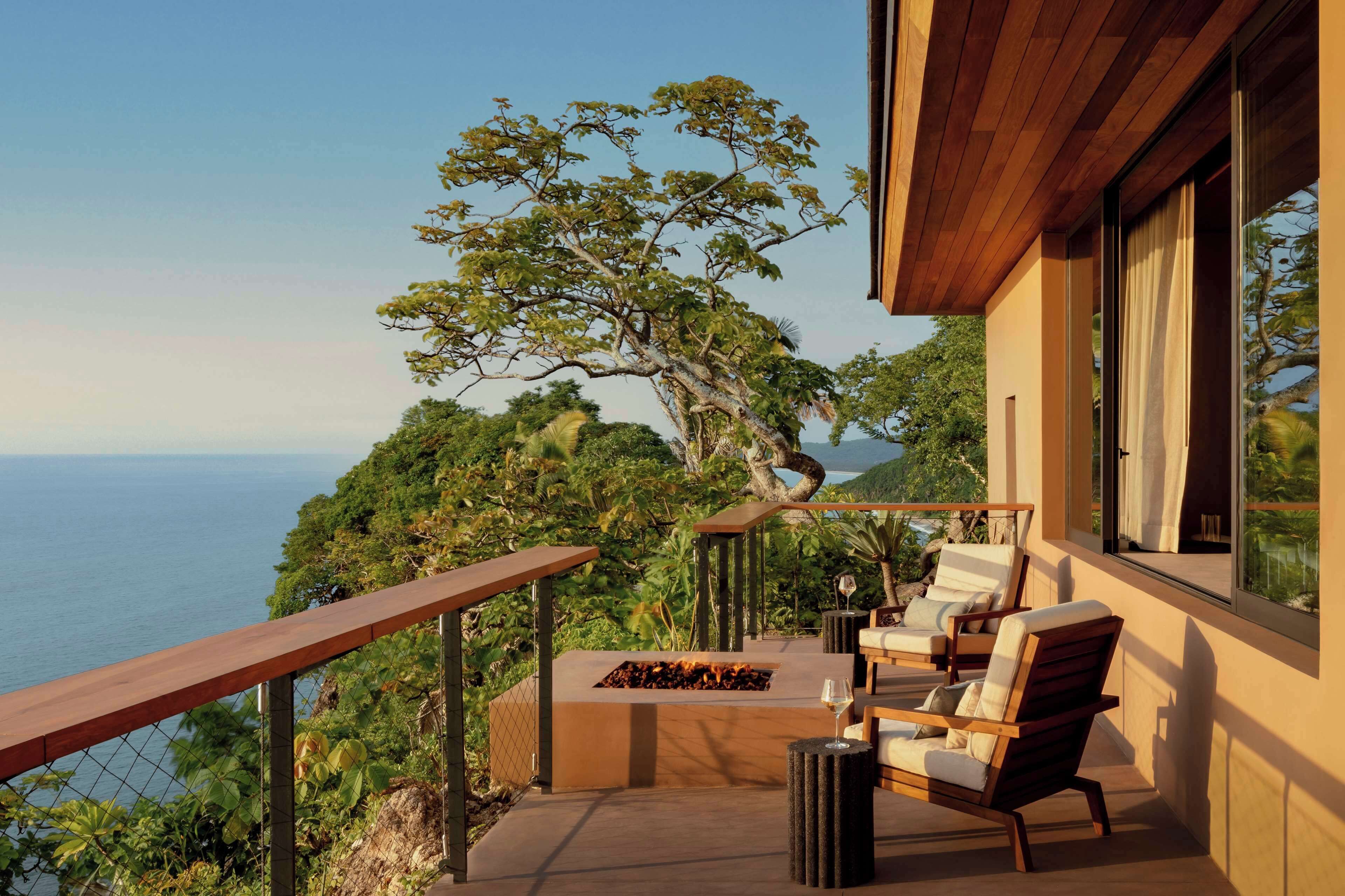 Un balcón con una chimenea, mobiliario exterior y vista al océano.