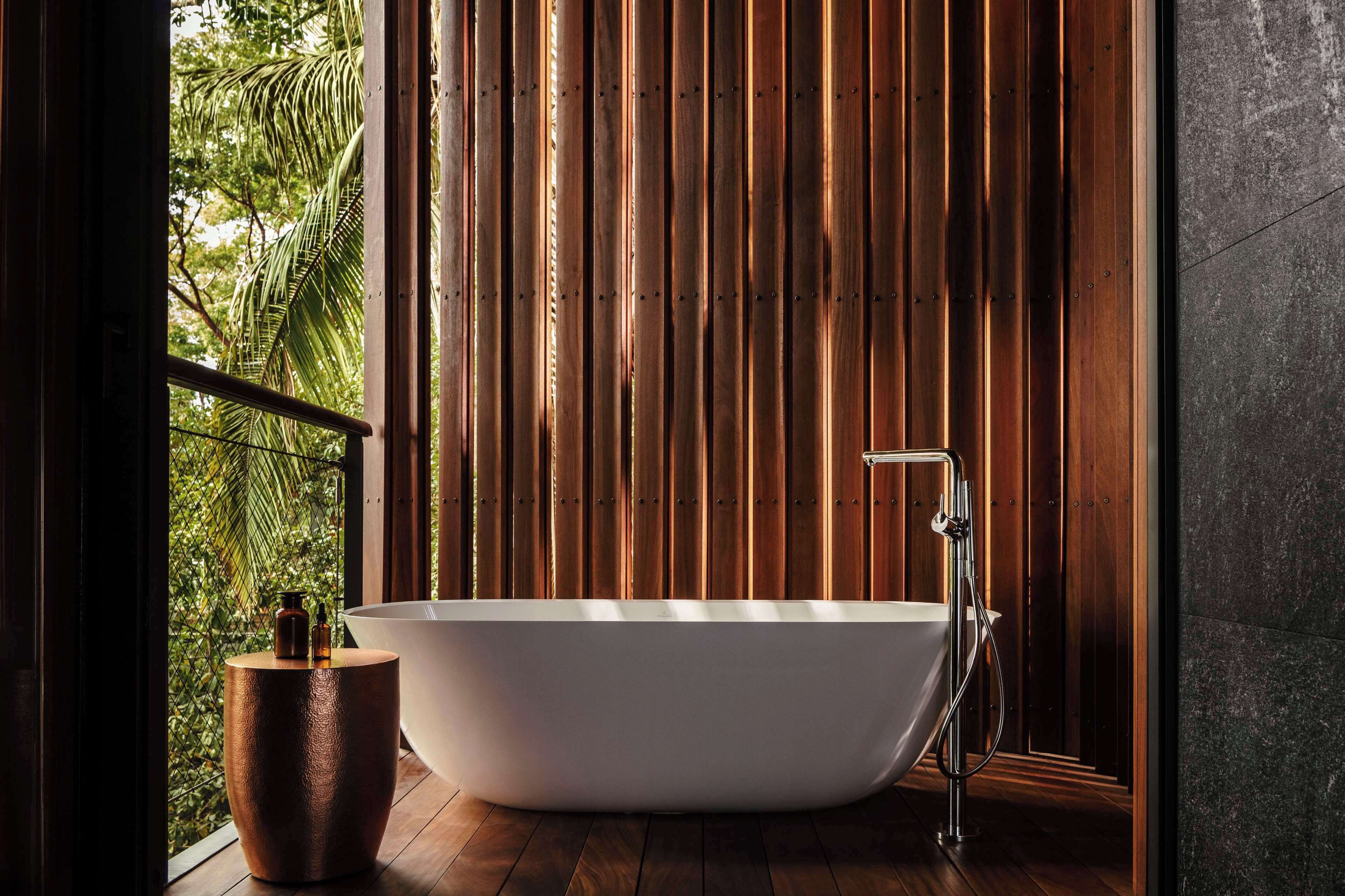 Un baño moderno con una bañera independiente, paneles de madera y vistas a la vegetación exterior.