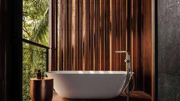 Un baño moderno con una bañera independiente, paneles de madera y vistas a la vegetación exterior.