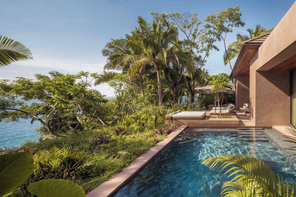 A swimming pool with a view of the ocean, surrounded by lush greenery and palm trees.