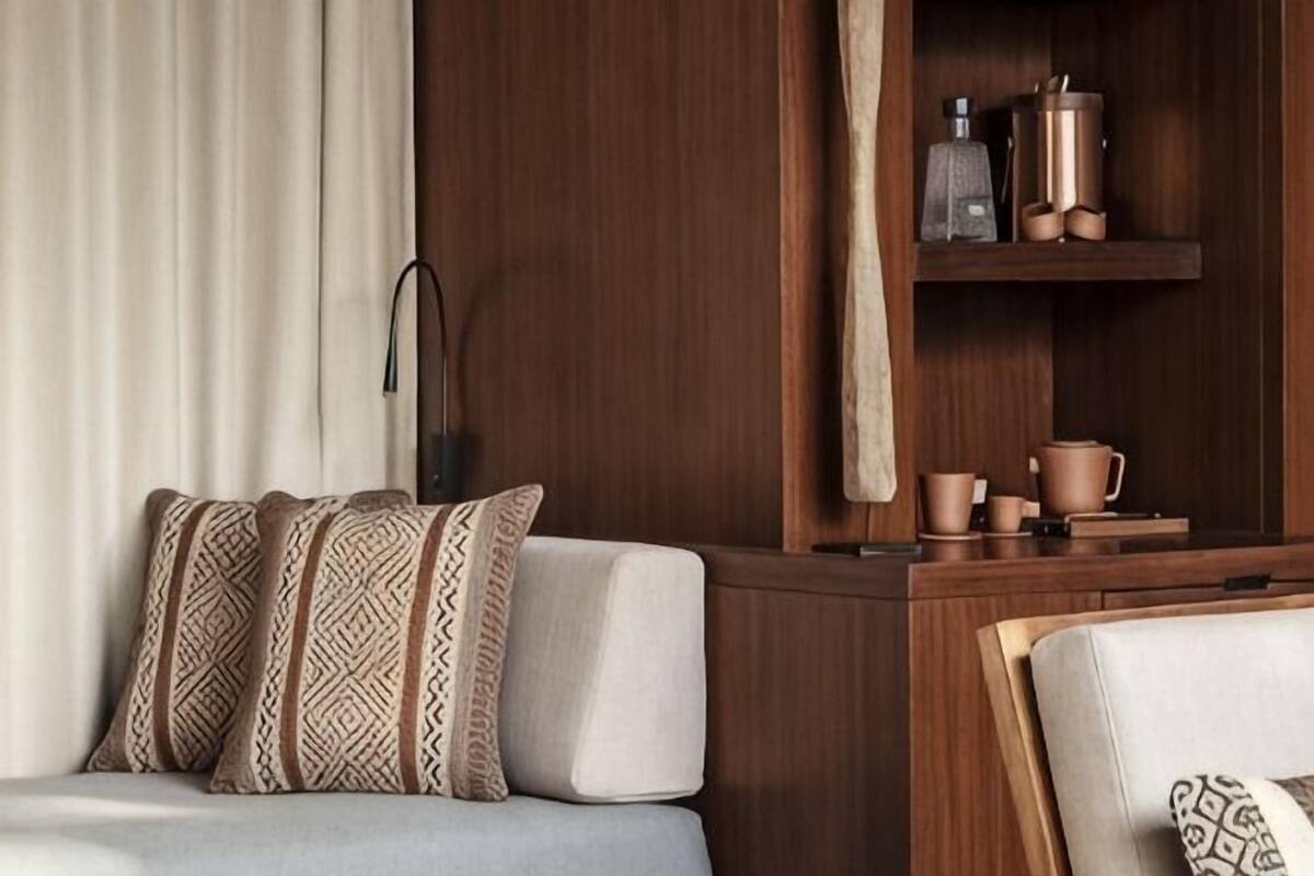 A room with a sofa, a wooden cabinet with kitchenware, and a lamp.