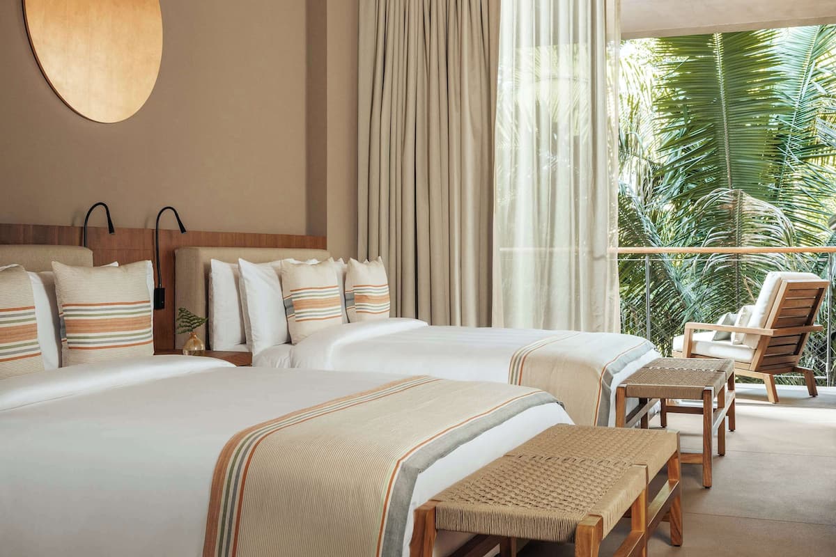 Habitación de hotel con una cama grande, ventilador de techo, vista a palmeras y un balcón con una silla.