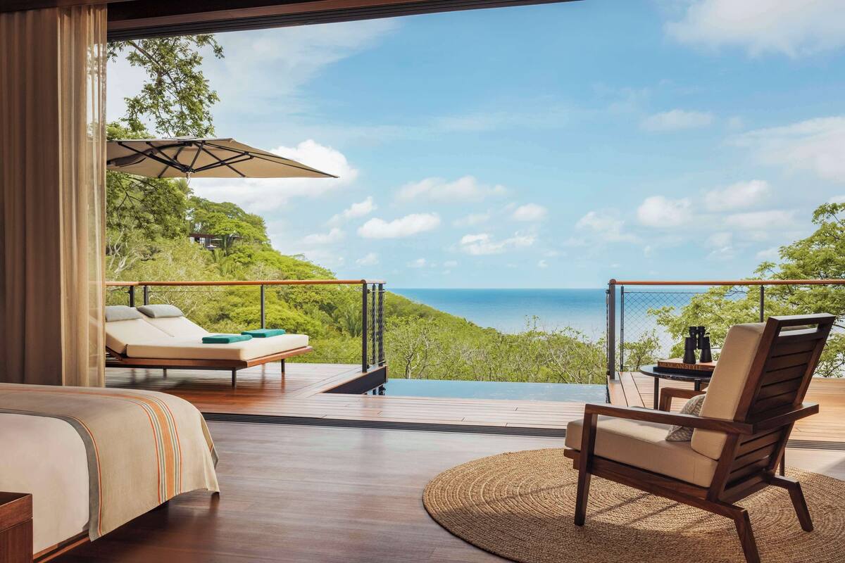A bedroom with a large window overlooking a scenic view of a lush green landscape and the sea.