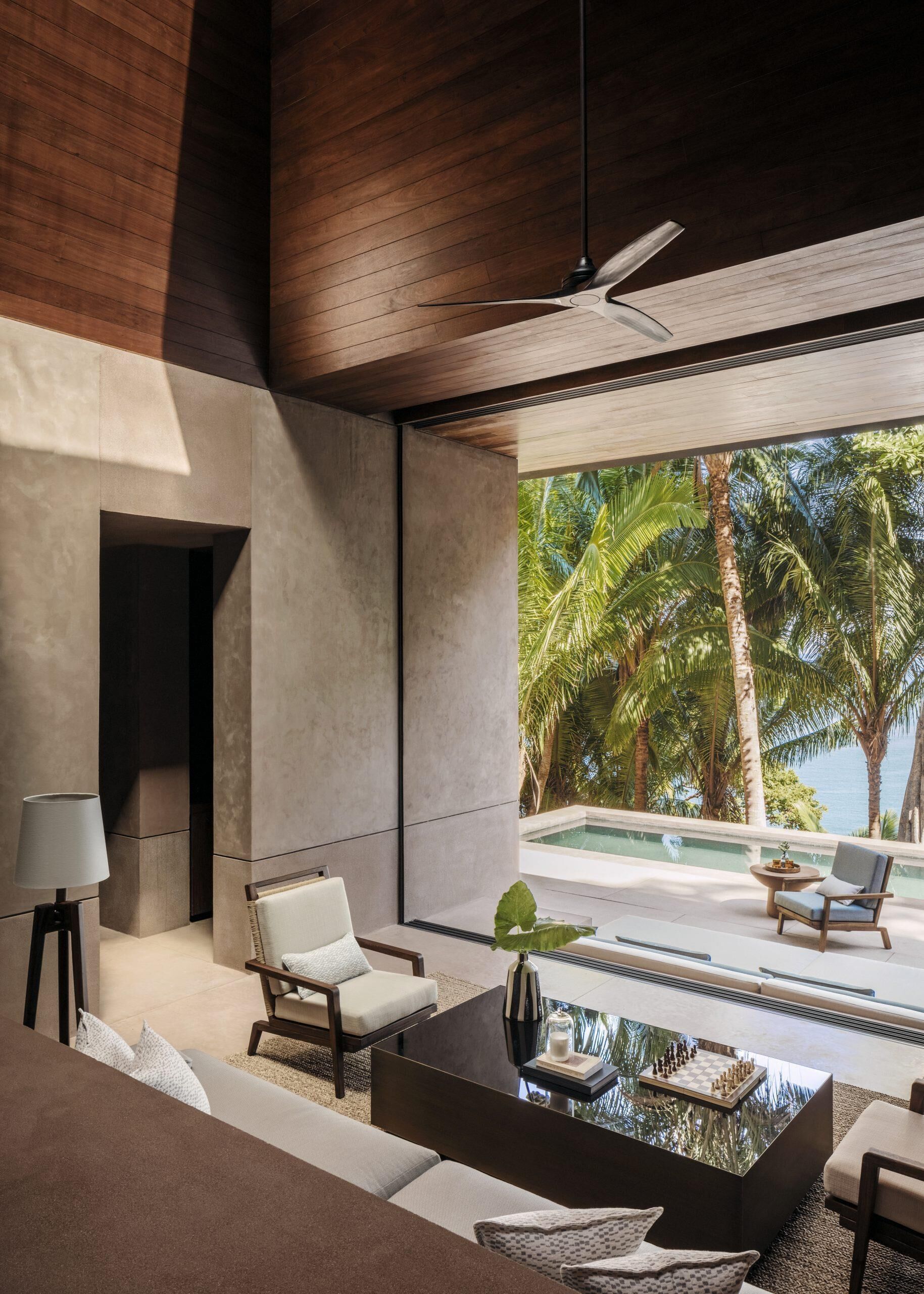 Una sala de estar moderna con un amplio ventanal que da a una piscina y palmeras.