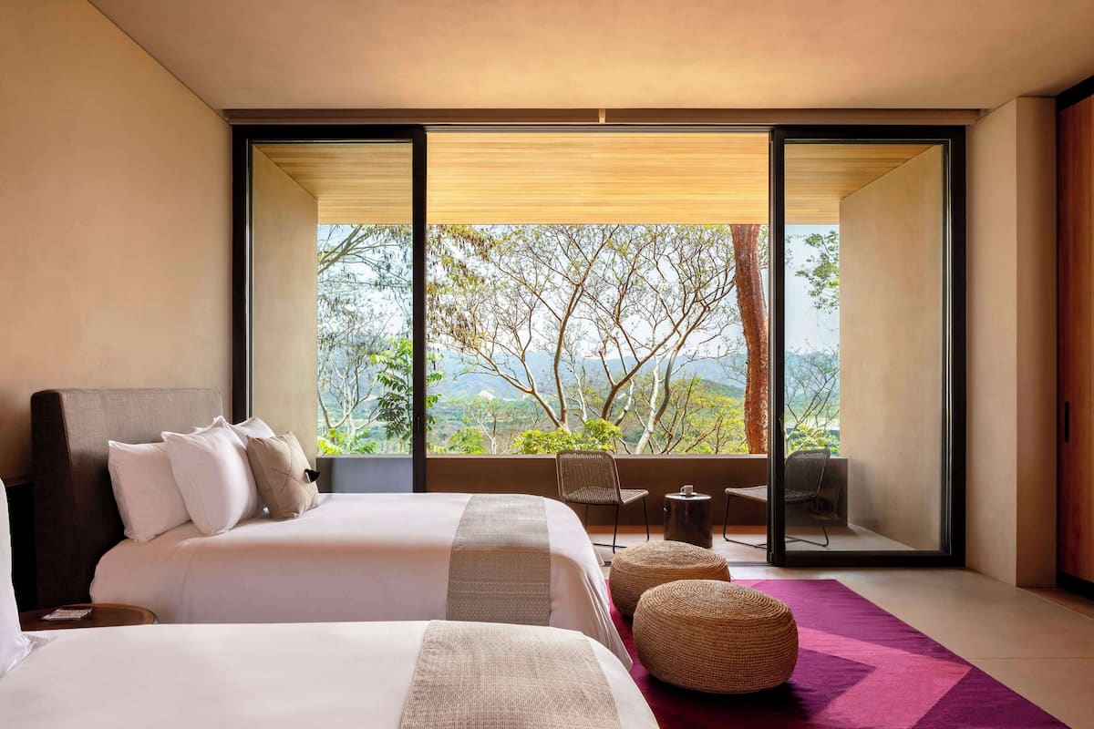Un dormitorio moderno con una cama grande, vistas al exterior y un balcón con mobiliario.