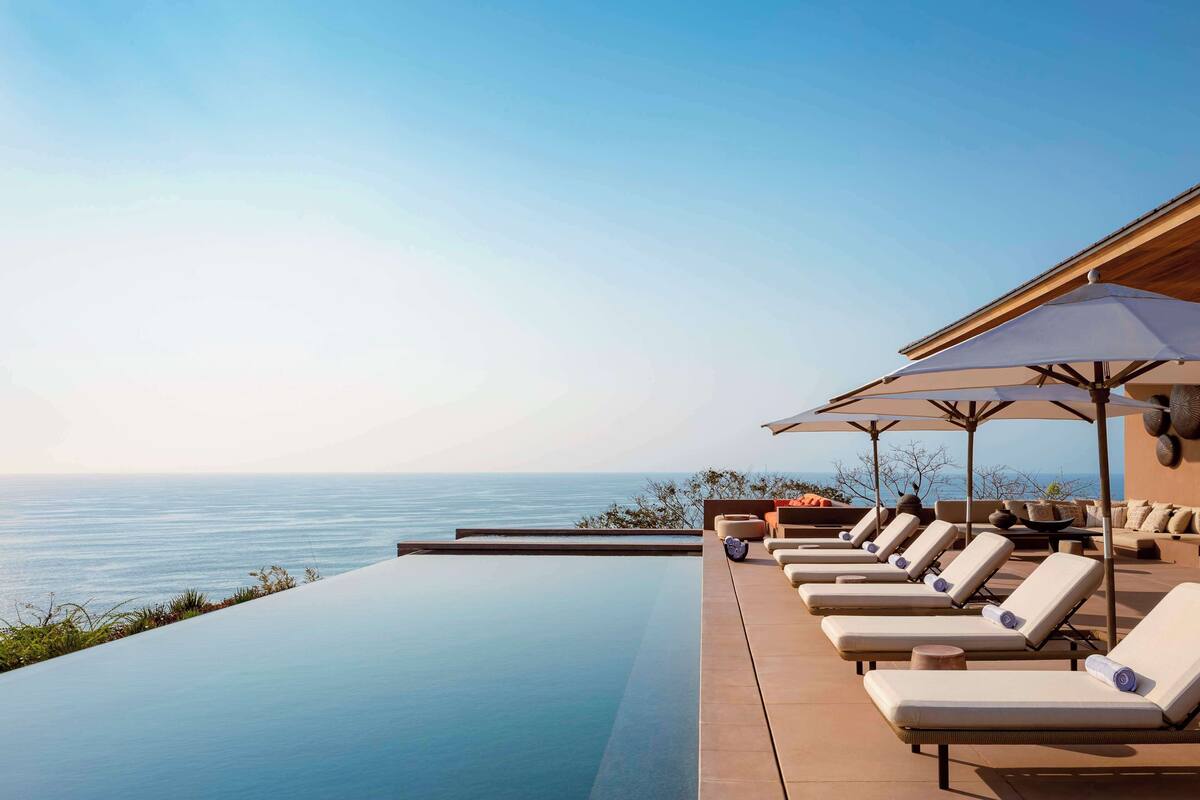 A poolside area with lounge chairs and umbrellas overlooking the sea.
