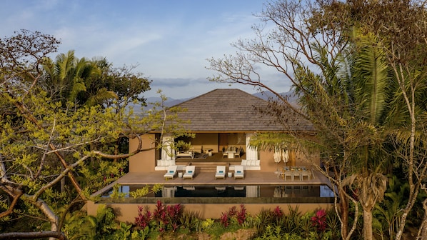 Una casa moderna con piscina, rodeada de exuberante vegetación y palmeras.