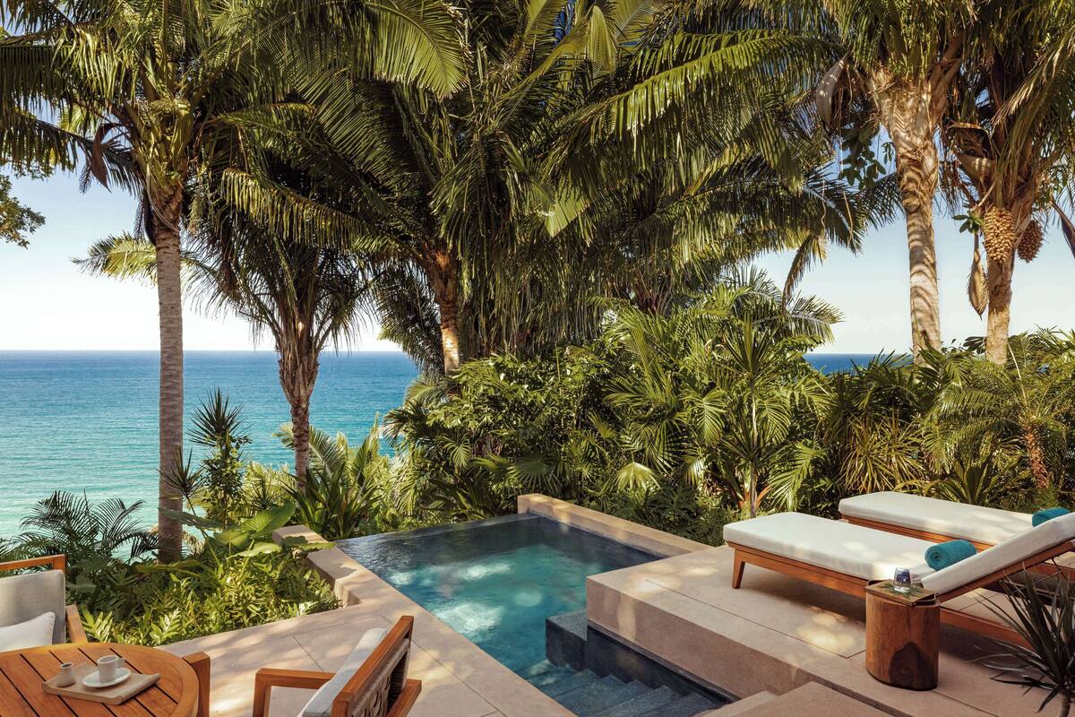 A pool area with lounge chairs and a view of the ocean.