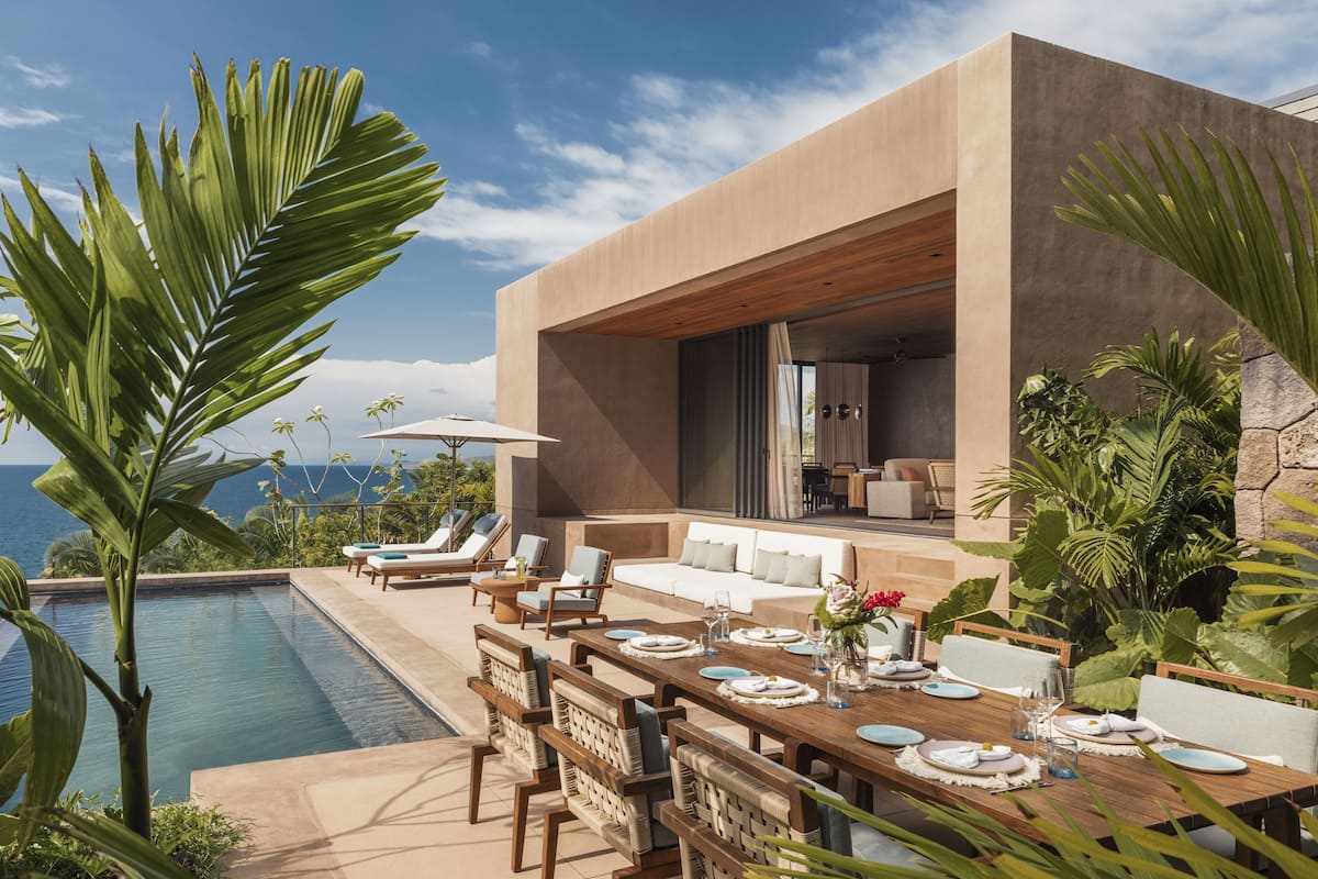 Un área de comedor moderna al aire libre con piscina, sillones de descanso y vistas al océano.