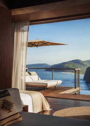 Camera con un'ampia finestra vista mare, un letto, una sedia e un ombrello.