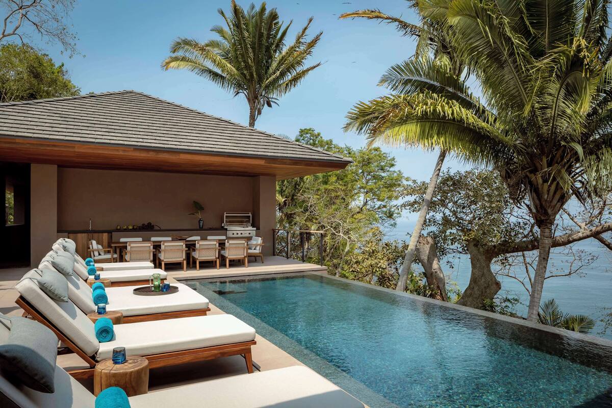 A poolside area with lounge chairs, a barbecue setup, and a view of the sea.