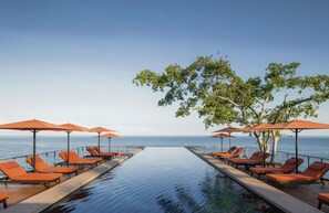 Un espace aménagé au bord de la piscine, avec des chaises longues et des parasols, offrant une vue sur la mer.