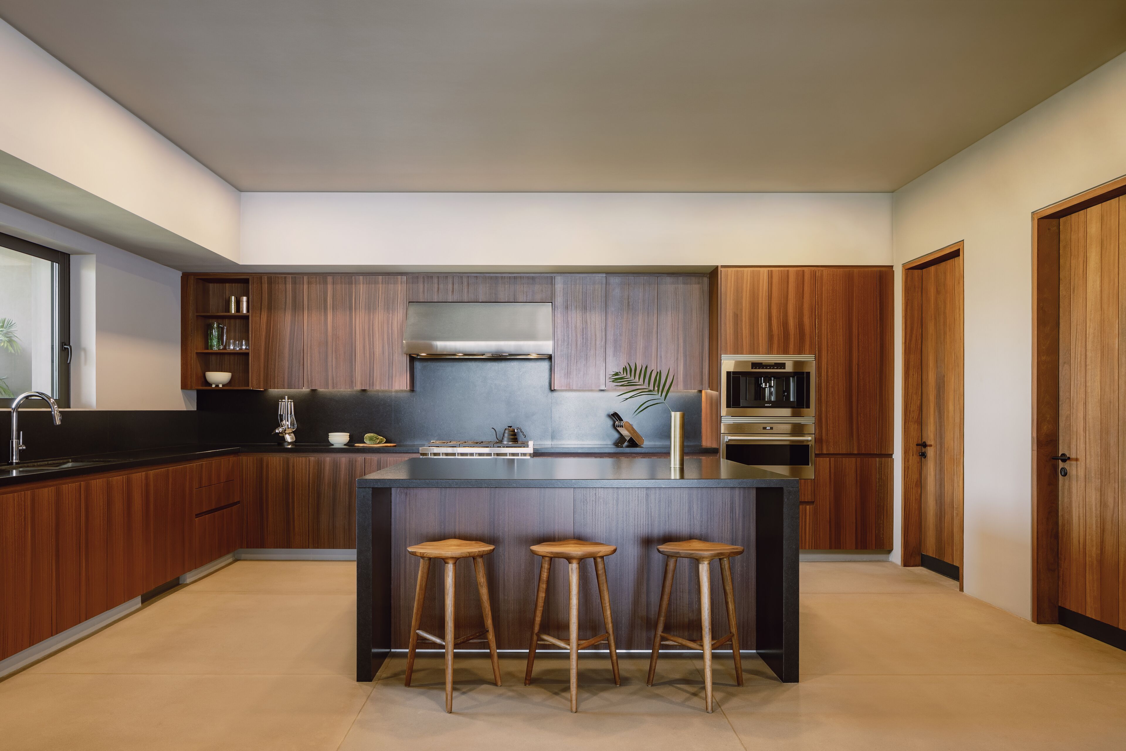 A modern kitchen with wooden cabinets, a central island with stools, a stainless steel range hood, and a built-in oven.