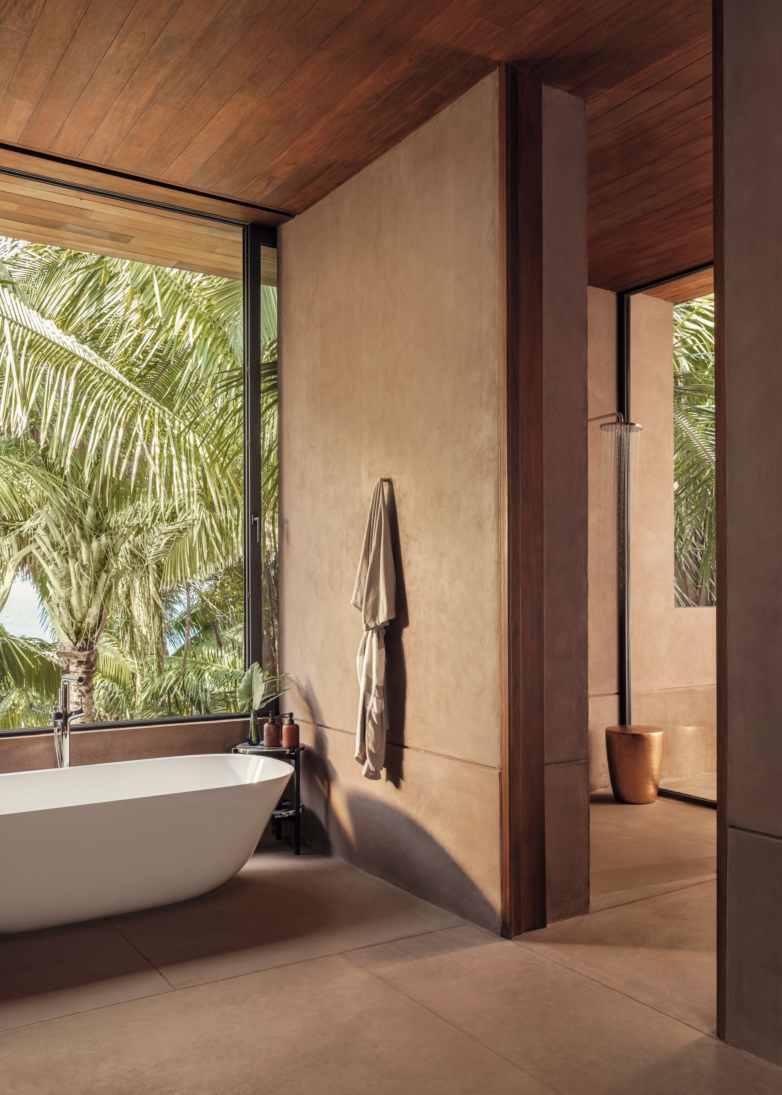 Un baño moderno con una bañera independiente, un perchero y un amplio ventanal con vistas a palmeras.
