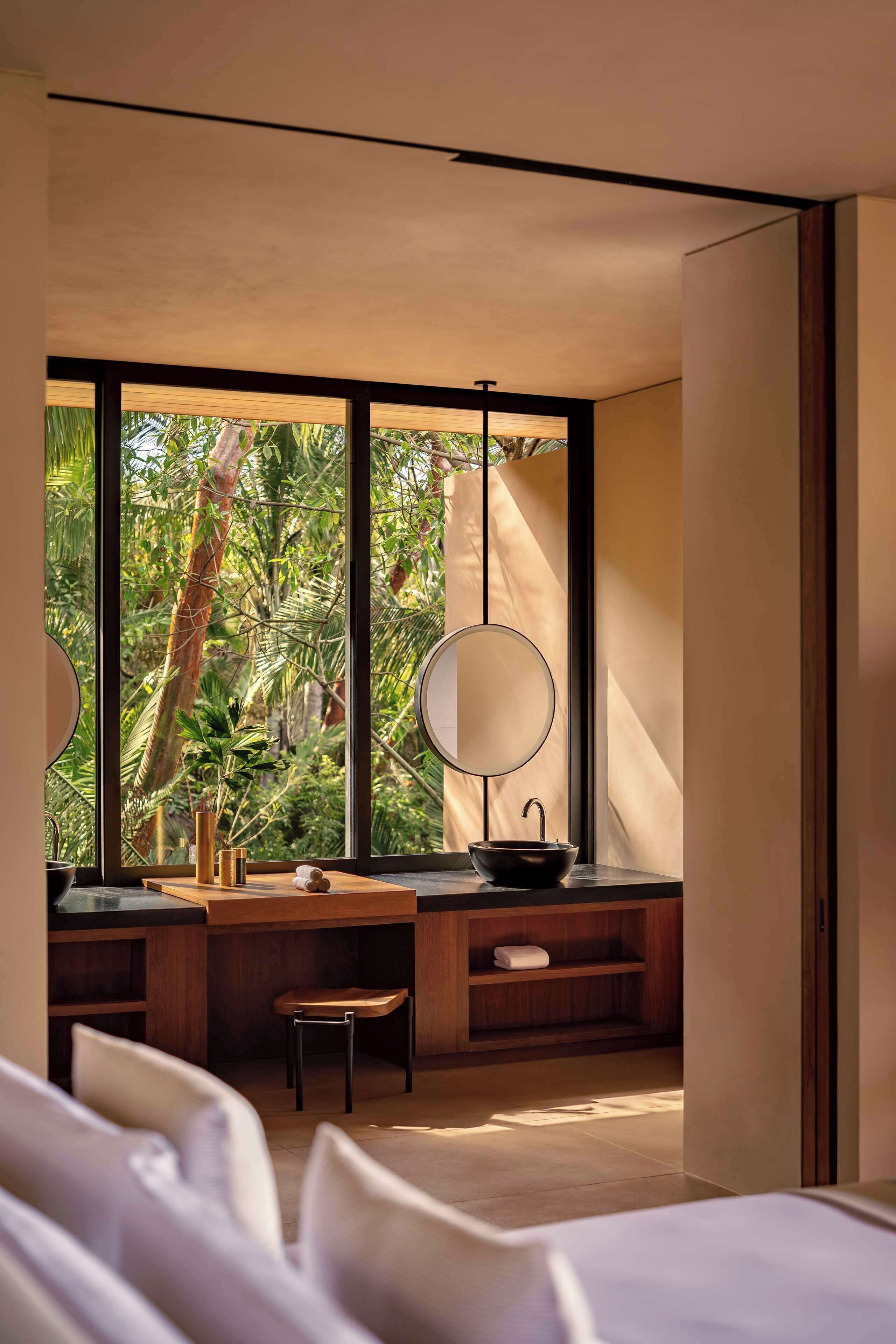 A modern bathroom with a large window, a round mirror, and a wooden vanity.