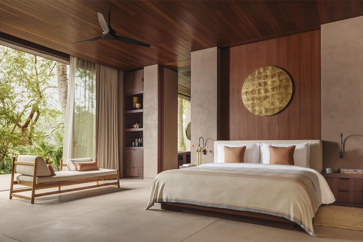Un dormitorio moderno con una cama grande, un ventilador de techo de madera, una estantería empotrada con adornos y vistas al exterior.