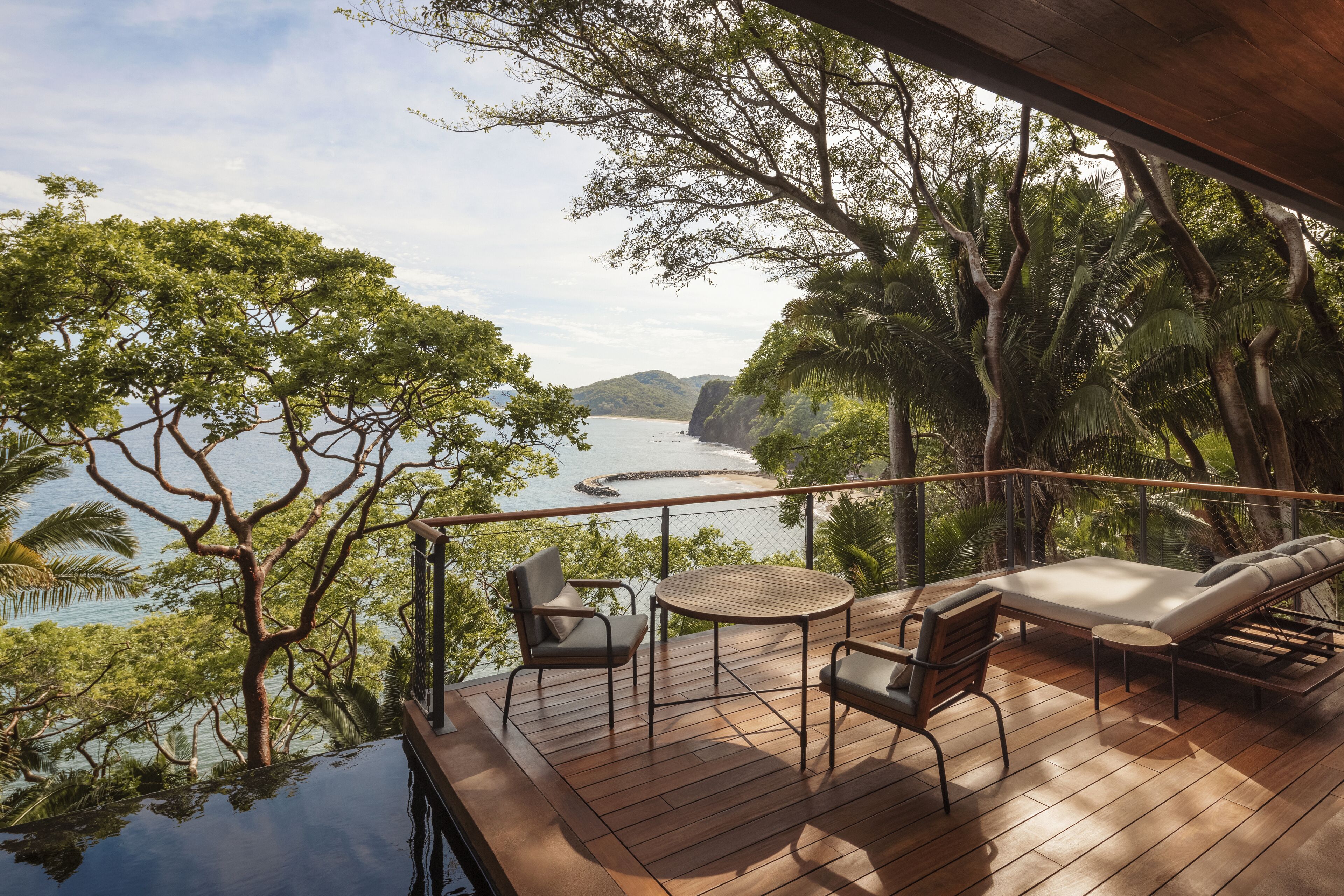 A wooden deck with a table and chairs, overlooking a body of water and lush greenery.