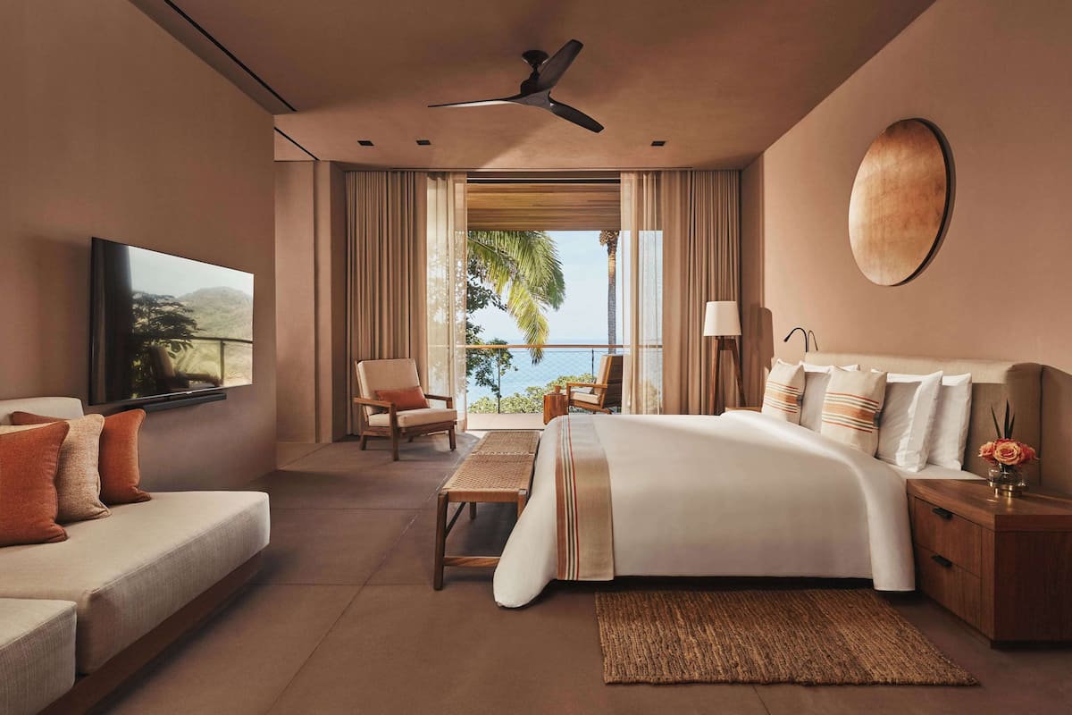 Una habitación de hotel moderna con una cama grande, un sofá, un televisor y un balcón con vistas.