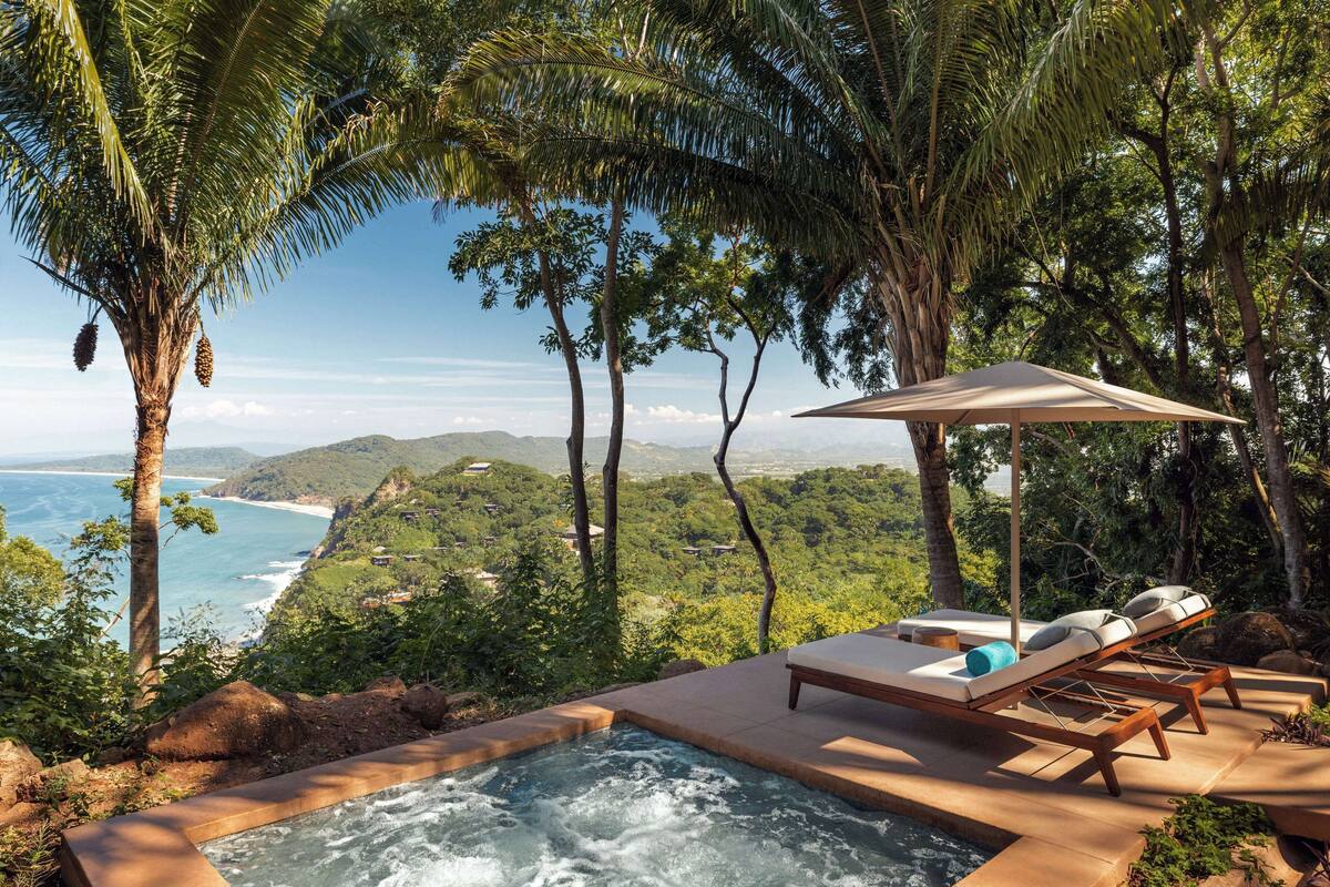 A hot tub with lounge chairs and an umbrella overlooking a coastal landscape.