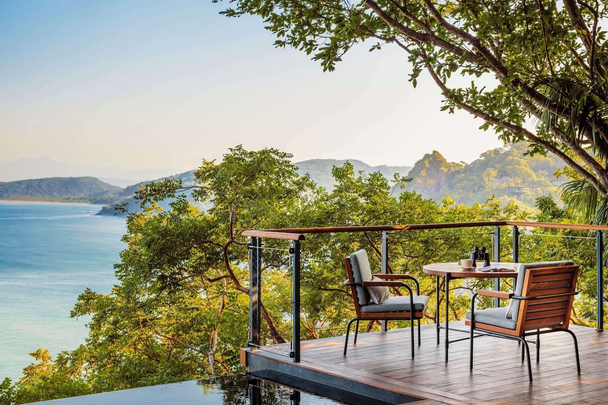 Una terraza con mesa y sillas con vista al agua y montañas.