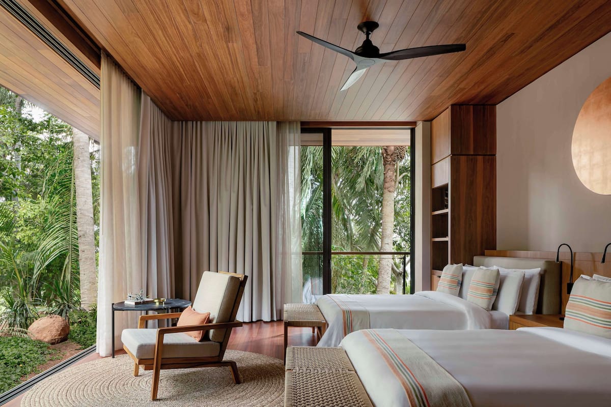 Una habitación de hotel moderna con techo de madera, ventanas amplias, una cama, una silla y una pequeña mesa.